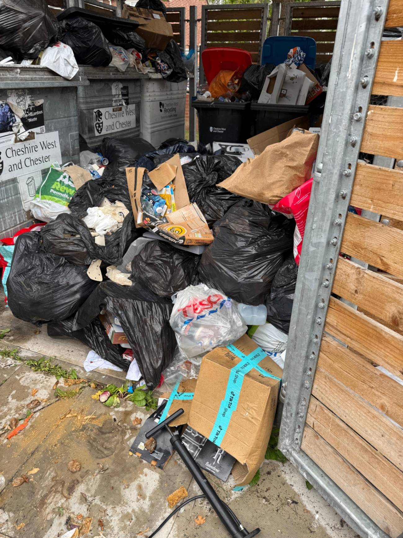 Overflowing communal bin store with fly tipped bagged waste piled outside Cheshire West and Chester bins