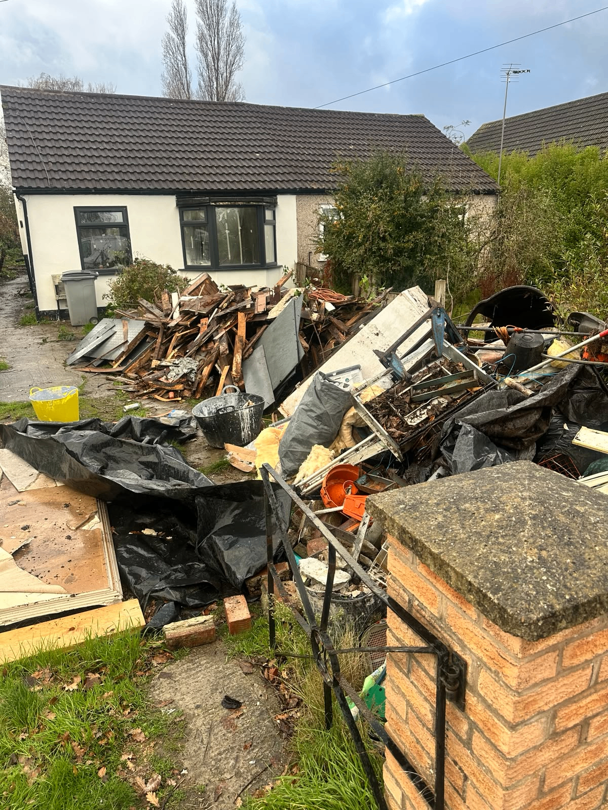 Before clearance: large pile of timber, plasterboard and builders' debris dumped in front of a bungalow