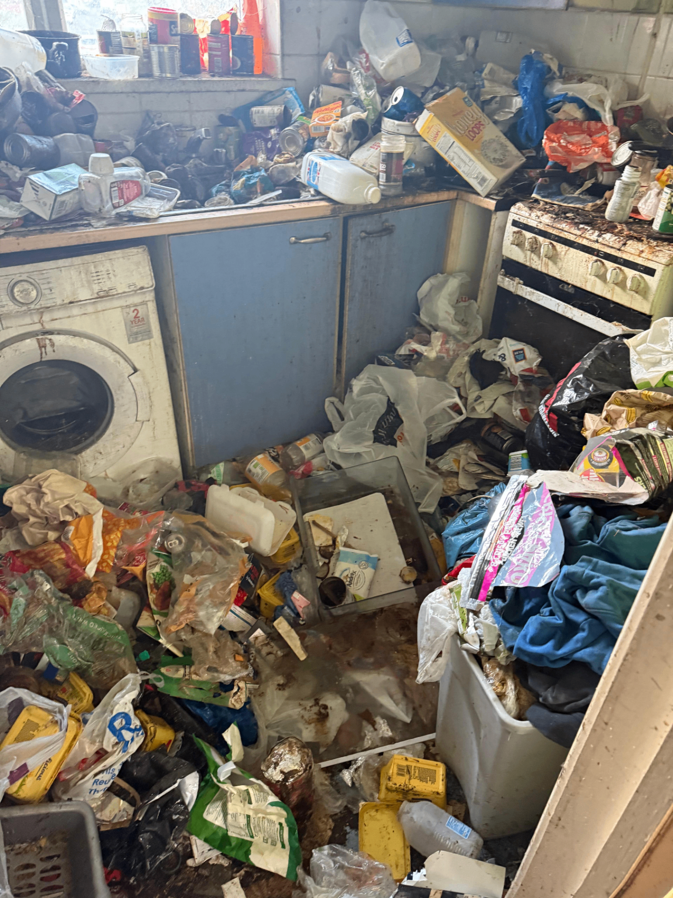 Kitchen floor and worktops covered in hoarded waste before clearance