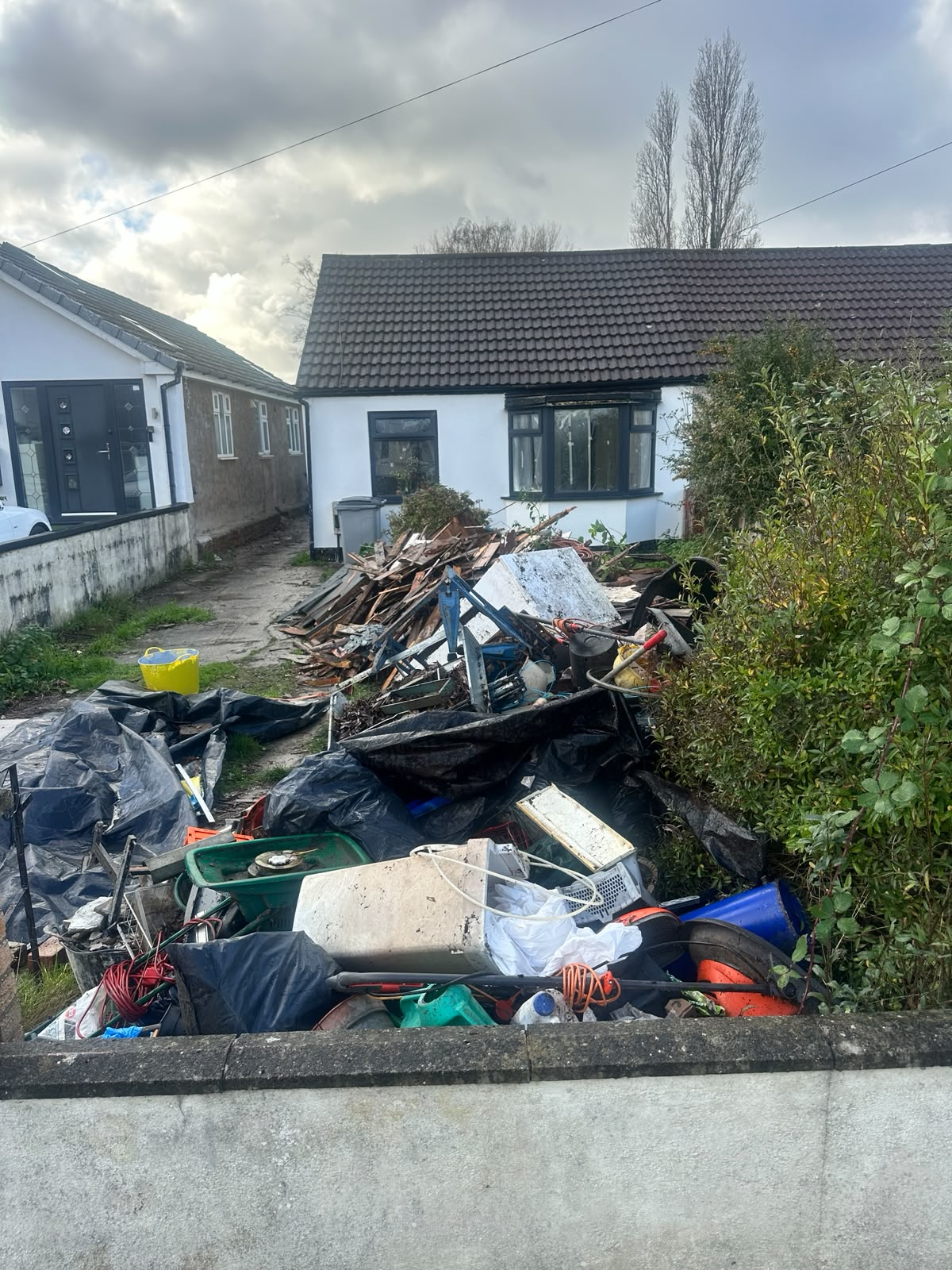Front garden piled with mixed waste, timber and debris before clearance